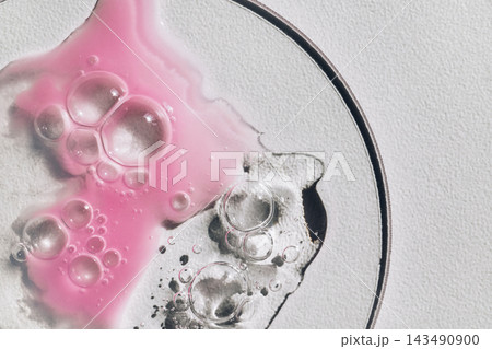 Pink and clear liquids mixing with bubbles on laboratory glass dish Pink and clear liquids mixing with bubbles on laboratory glass dish 143490900
