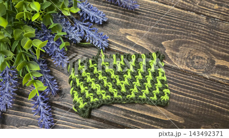 Knitted swatch with two-tone green geometric pattern on dark wooden background 143492371