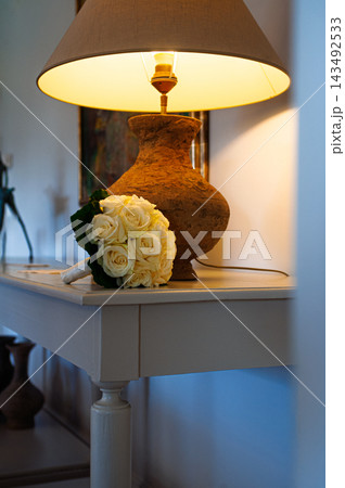 Wedding Bouquet of Cream Roses on a Console Table Beside a Warm Lit Lamp in a Cozy Home Interior Wedding Bouquet of Cream Roses on a Console Table Beside a Warm Lit Lamp in a Cozy Home Interior 143492533