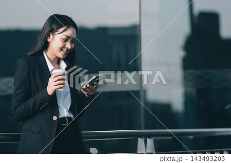 Smiling young corporate woman looking at her smartphone while sitting outdoors in the city 143493203