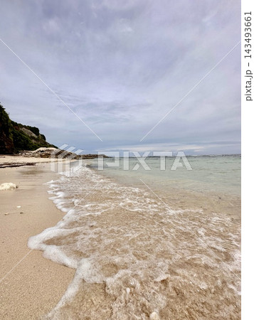 Gentle turquoise surf spreads across pale sand beneath coastal cliffs and cloudy skies. Gentle turquoise surf spreads across pale sand beneath coastal cliffs and cloudy skies. 143493661