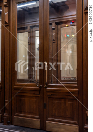 Ornate Wooden Double Entrance Door With Brass Handles and Glass Panels in Elegant Interior Ornate Wooden Double Entrance Door With Brass Handles and Glass Panels in Elegant Interior 143493756