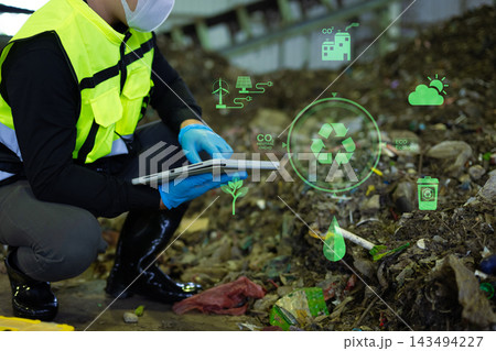 Asian engineer in hardhat using tablet with green energy and carbon neutral HUD graphics inside recycling factory Asian engineer in hardhat using tablet with green energy and carbon neutral HUD graphics inside recycling factory 143494227