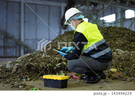 Industrial worker in safety gear using a tablet to inspect organic waste at a recycling facility. Promoting sustainability Industrial worker in safety gear using a tablet to inspect organic waste at a recycling facility. Promoting sustainability 143494229