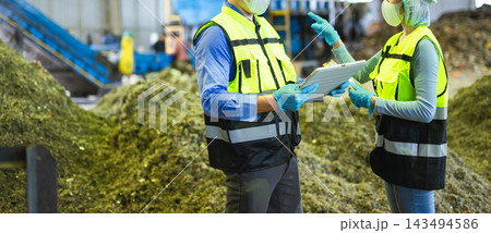 Midsection of two industrial workers in safety vests using a digital tablet to inspect organic waste processing and sorting 143494586