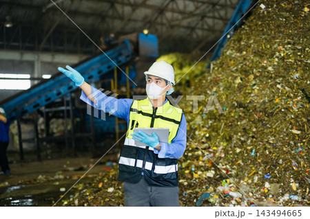 Quality inspector using digital tablet near conveyor belt and garbage pile inside municipal recycling plant. Quality inspector using digital tablet near conveyor belt and garbage pile inside municipal recycling plant. 143494665