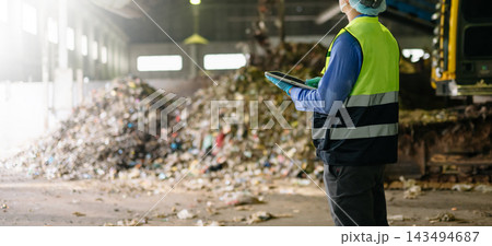 Quality inspector in hardhat and mask taking notes beside a large compost pile, evaluating organic waste management 143494687