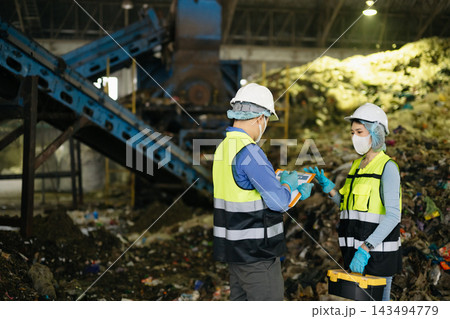 Industrial engineers in safety gear inspect recycling machinery and organic waste sorting processes at modern green energy factory facility. 143494779