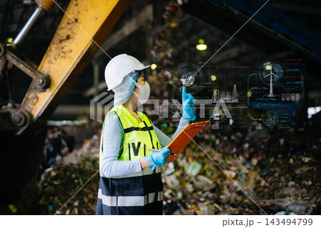Quality inspector using digital tablet near conveyor belt and garbage pile inside municipal recycling plant. 143494799