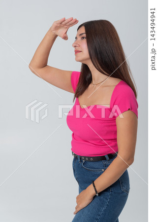 Young woman standing in profile, shielding her eyes with a hand while looking intently into the distance, conveying concepts of searching, discovery, and anticipation 143494941