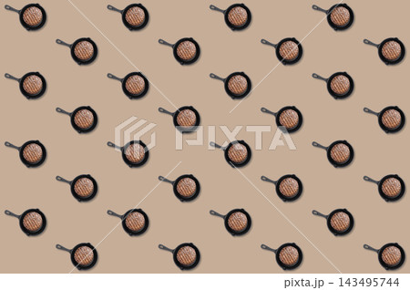 Small black skillets with grilled burger patties repeated in diagonal rows across a beige food pattern background 143495744