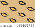 Repeating pattern of baked ocean perch fillets in black oval handled dishes arranged on a warm golden background 143495752