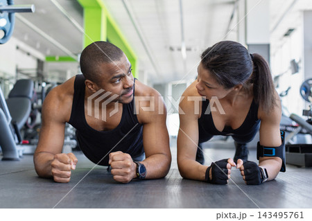 Black couple holding plank position on gym floor, looking at each other Black couple holding plank position on gym floor, looking at each other 143495761