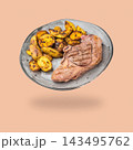 Grilled lamb chop with roasted potatoes on a gray plate floating above a soft shadow on a peach background 143495762