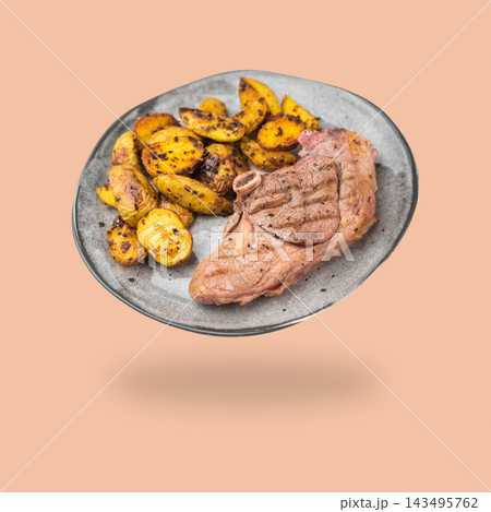 Grilled lamb chop with roasted potatoes on a gray plate floating above a soft shadow on a peach background Grilled lamb chop with roasted potatoes on a gray plate floating above a soft shadow on a peach background 143495762