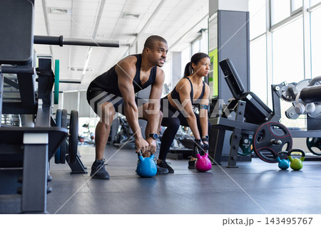 Athletic black man and woman performing kettlebell deadlift exercises together in gym 143495767