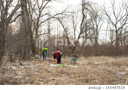 Community members working together to clean up a natural area during late afternoon in early spring, promoting environmental awareness and teamwork 143497619