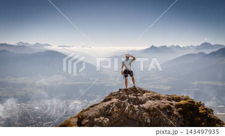 Solo male mountaineer standing on a rocky summit overlooking the Austrian Alps near Innsbruck, experiencing a moment of freedom, achievement and inspiration above the vast alpine landscape. 143497935