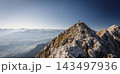 Hiker standing on a rocky summit during a via ferrata in the Austrian Alps near Innsbruck, Tyrol, with dramatic mountain peaks and a vast alpine landscape in the background. 143497936