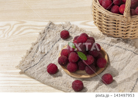 Fresh ripe red bayberries on a small wooden plate and in a wicker basket on a wooden table background 143497953