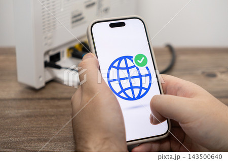 A person holds a smartphone displaying a globe icon with a checkmark to verify a successful internet router connection, symbolizing network stability and reliable high speed connectivity A person holds a smartphone displaying a globe icon with a checkmark to verify a successful internet router connection, symbolizing network stability and reliable high speed connectivity 143500640