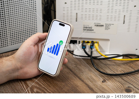 A person holds a smartphone displaying a full wifi signal icon next to a white home internet router, representing successful network setup, high speed connectivity, and digital access A person holds a smartphone displaying a full wifi signal icon next to a white home internet router, representing successful network setup, high speed connectivity, and digital access 143500689