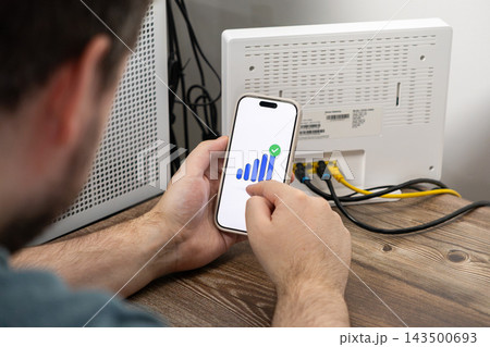 A person checks their strong wifi signal strength on a smartphone app screen next to a home router to ensure reliable network connectivity for remote work and digital management A person checks their strong wifi signal strength on a smartphone app screen next to a home router to ensure reliable network connectivity for remote work and digital management 143500693
