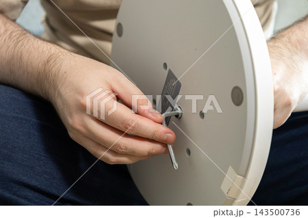 A person assembling furniture by tightening a metal bolt with an Allen key into a white circular base, demonstrating home improvement and DIY assembly skills in a domestic environment A person assembling furniture by tightening a metal bolt with an Allen key into a white circular base, demonstrating home improvement and DIY assembly skills in a domestic environment 143500736