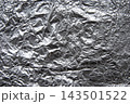 Silver crumpled foil texture background. An abstract metallic shiny surface with folds and glares macro photo 143501522