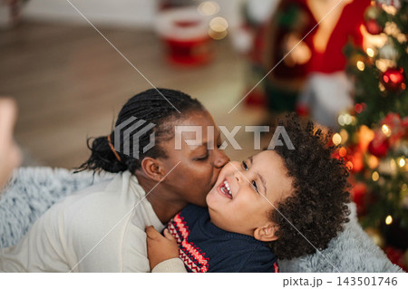 Mother kissing laughing son at Christmas holiday Mother kissing laughing son at Christmas holiday 143501746