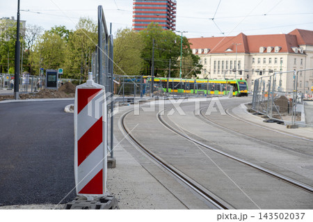 A red and white barrier stands by city tram tracks during urban construction works, defining a zone for road improvement projects in a metropolitan area near transit infrastructure 143502037