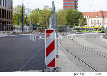 A red and white traffic sign stands by tram tracks under construction in a city, signaling caution and barriers during urban renovation work to improve public transport infrastructure A red and white traffic sign stands by tram tracks under construction in a city, signaling caution and barriers during urban renovation work to improve public transport infrastructure 143502038