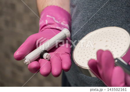 A hand in a pink rubber glove holds a replacement shower water filter cartridge and a head, illustrating maintenance for clean bathroom plumbing and improved home hygiene lifestyle 143502161