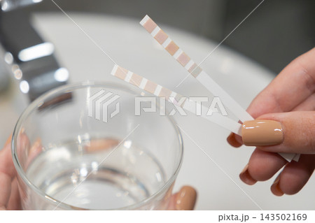 A hand holding two test strips for checking water quality in a glass, representing laboratory analysis, home health assessment, safety monitoring, and environmental testing practices A hand holding two test strips for checking water quality in a glass, representing laboratory analysis, home health assessment, safety monitoring, and environmental testing practices 143502169
