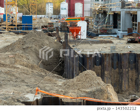 A construction site featuring deep excavation trenches and metal shoring walls, establishing a busy industrial scene for urban infrastructure development and large real estate builds 143502212