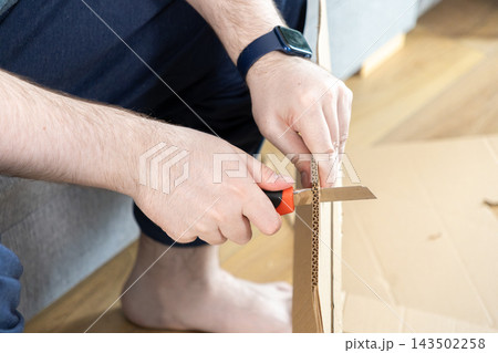 Person using a utility knife to cut corrugated cardboard in a home setting, illustrating manual DIY projects, packing tasks, crafting hobbies, and effective household improvement work Person using a utility knife to cut corrugated cardboard in a home setting, illustrating manual DIY projects, packing tasks, crafting hobbies, and effective household improvement work 143502258