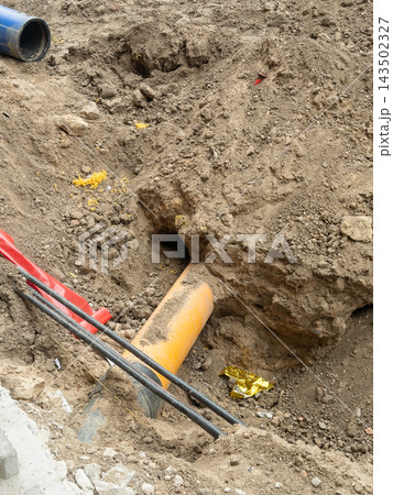 A construction site trench reveals plastic pipes laid in excavated soil during utility installation work, representing urban development, infrastructure projects, and engineering A construction site trench reveals plastic pipes laid in excavated soil during utility installation work, representing urban development, infrastructure projects, and engineering 143502327
