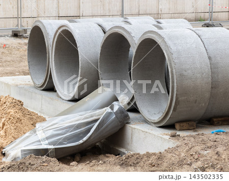 Large concrete drainage pipes stacked at a busy urban construction site, providing essential infrastructure materials for municipal sewer system expansion projects in a growing city Large concrete drainage pipes stacked at a busy urban construction site, providing essential infrastructure materials for municipal sewer system expansion projects in a growing city 143502335