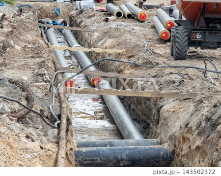 Industrial pipeline construction trench featuring metal conduit laying in an excavated dirt ground site, symbolizing utility infrastructure development and modern civil engineering work Industrial pipeline construction trench featuring metal conduit laying in an excavated dirt ground site, symbolizing utility infrastructure development and modern civil engineering work 143502372