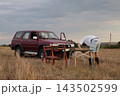 Person sets up tables near parked SUV in an field. 143502599