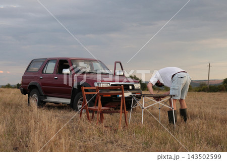 Person sets up tables near parked SUV in an field. Person sets up tables near parked SUV in an field. 143502599