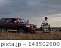 Man stands near brown SUV on open field. 143502600