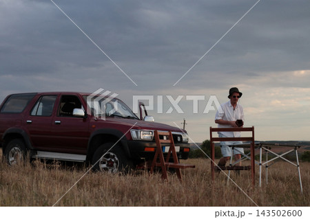 Man stands near brown SUV on open field. 143502600