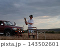 Man stands near brown SUV on open field. 143502601
