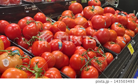 ripe red tomatoes on the vine on a supermarket display. A neat arrangement of juicy tomatoes with price tags in the store's produce section. 143503493