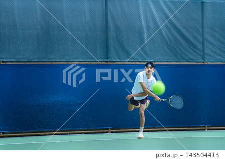 Young Asian Male Tennis Player Hitting a Powerful Serve on Outdoor Court 143504413