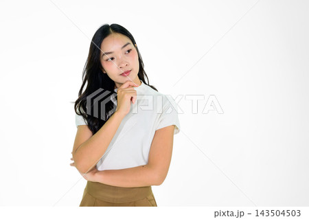 Thoughtful Young Asian Girl Posing Against White Background with Hand on Chin in Casual Outfit 143504503