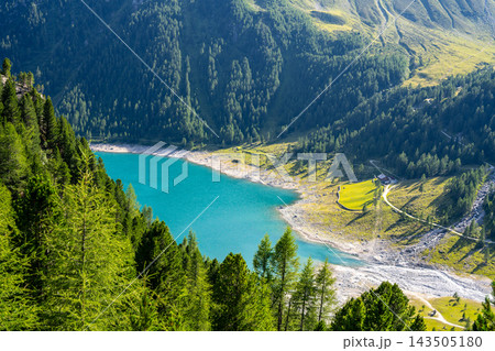 Lake Neves is in South Tyrol at the end of the Molini Valley in the Zillertal Alps. This view shows the clear water and surrounding green trees on a sunny day. Lake Neves is in South Tyrol at the end of the Molini Valley in the Zillertal Alps. This view shows the clear water and surrounding green trees on a sunny day. 143505180