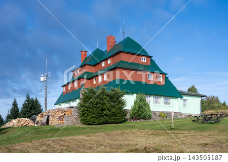 This is Masaryk's cottage located on Serlich. It is a well-known mountain cottage in the Orlicke ountains. The structure features multiple roofs and is surrounded by grass and trees. 143505187