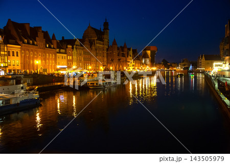 Evening view of Gdansk's waterfront with illuminated buildings and boats along the river Evening view of Gdansk's waterfront with illuminated buildings and boats along the river 143505979